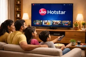 Indian family of four sitting on a sofa watching JioHotstar on a smart TV in a cozy living room with warm lighting.